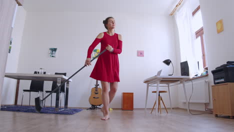 Happy-girl-dancing-with-broom-cleaning-floor-and-enjoying-housework,-low-angle-slider-view