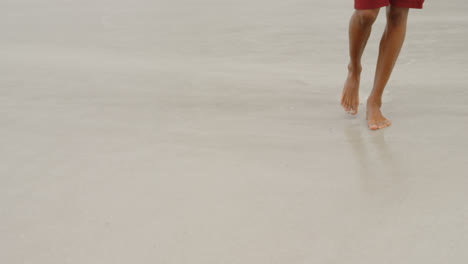 sección baja de un hombre caminando descalzo en la playa en un día soleado 4k