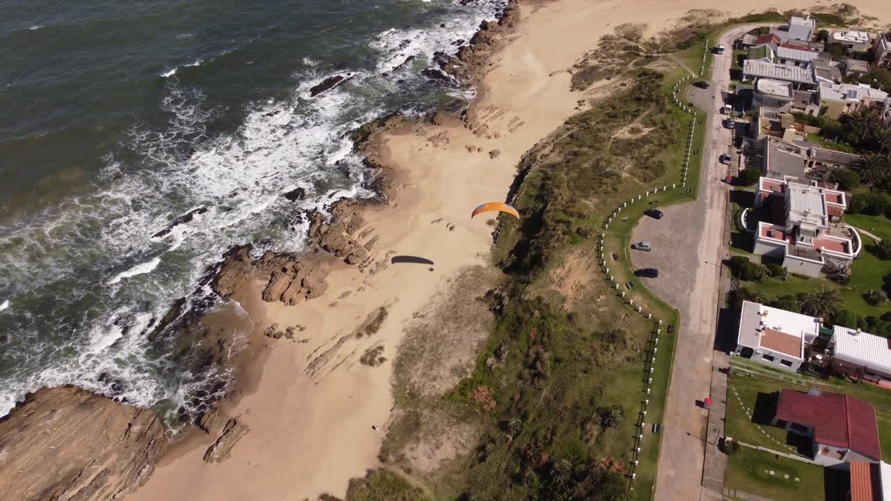 antena que muestra a un turista disfrutando del parapente desde los acantilados junto a la playa en el pueblo de la pedrera en la costa atlántica, uruguay