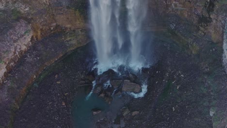 A-waterfall-cascading-into-a-rocky-pool-in-a-serene-forest-setting,-aerial-view