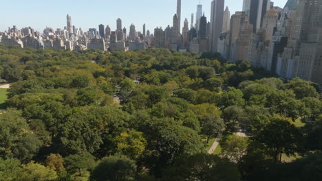 Flying-over-a-building,-revealing-the-sunny-Central-park-of-New-York---Aerial-view