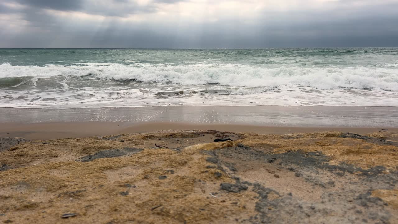 해변을 향해 찍은 사진으로, 흐린 날의 부드러운 햇살 아래 잔잔한 파도가 모래사장으로 밀려오는 모습을 담고 있어요.
