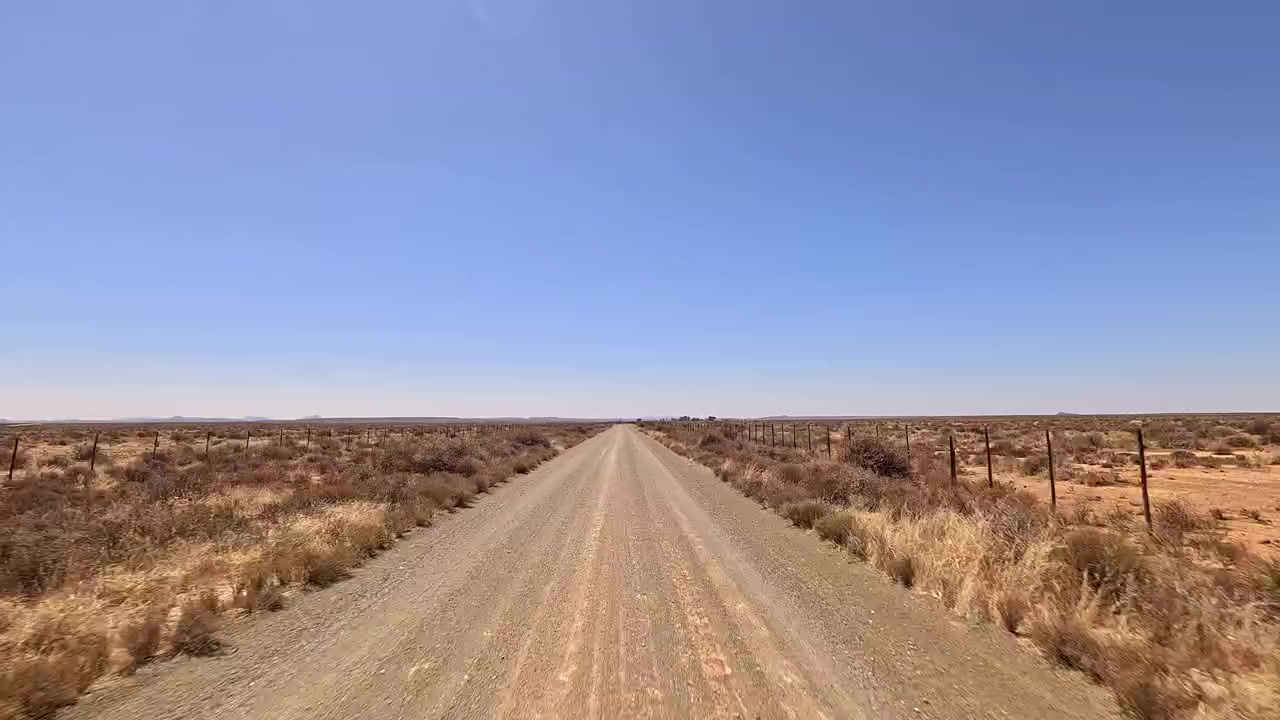 Açık gökyüzü altında çorak bir çölün içinden uzanan düz toprak yol.