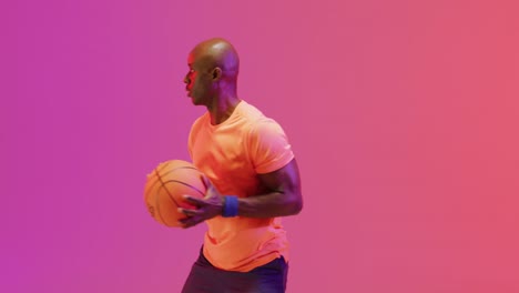 Video-of-african-american-male-basketball-player-throwing-ball-on-pink-to-orange-background