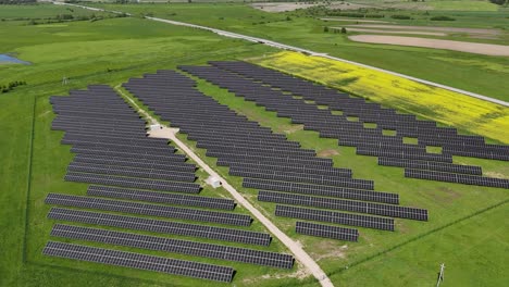 Una-Gran-Granja-De-Paneles-Solares-En-Un-Campo-Verde-En-Un-Día-Soleado,-Vista-Aérea