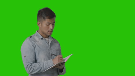 male university or college student taking notes in lecture or lesson against green screen