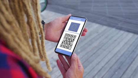 man with dreadlocks holding smartphone, covid vaccination certificate, eu flag and qr code on screen