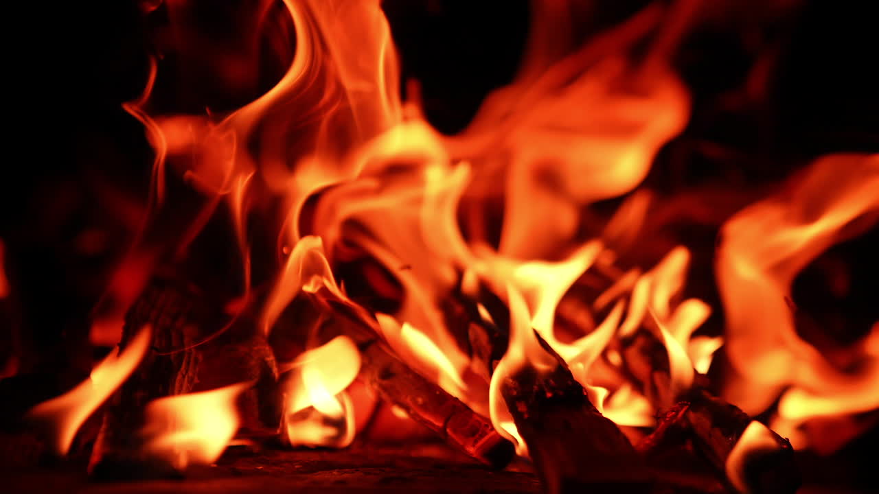 Wooden logs turning into charcoal in the campfire. Close up view on the fire flames at black backdrop.