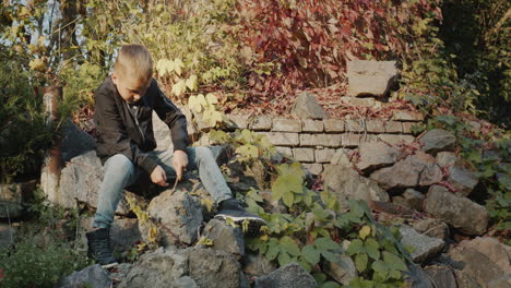 The-boy-plays-in-the-park---sits-on-the-rocks-and-picks-the-ground-with-a-stick.-Carefree-childhood