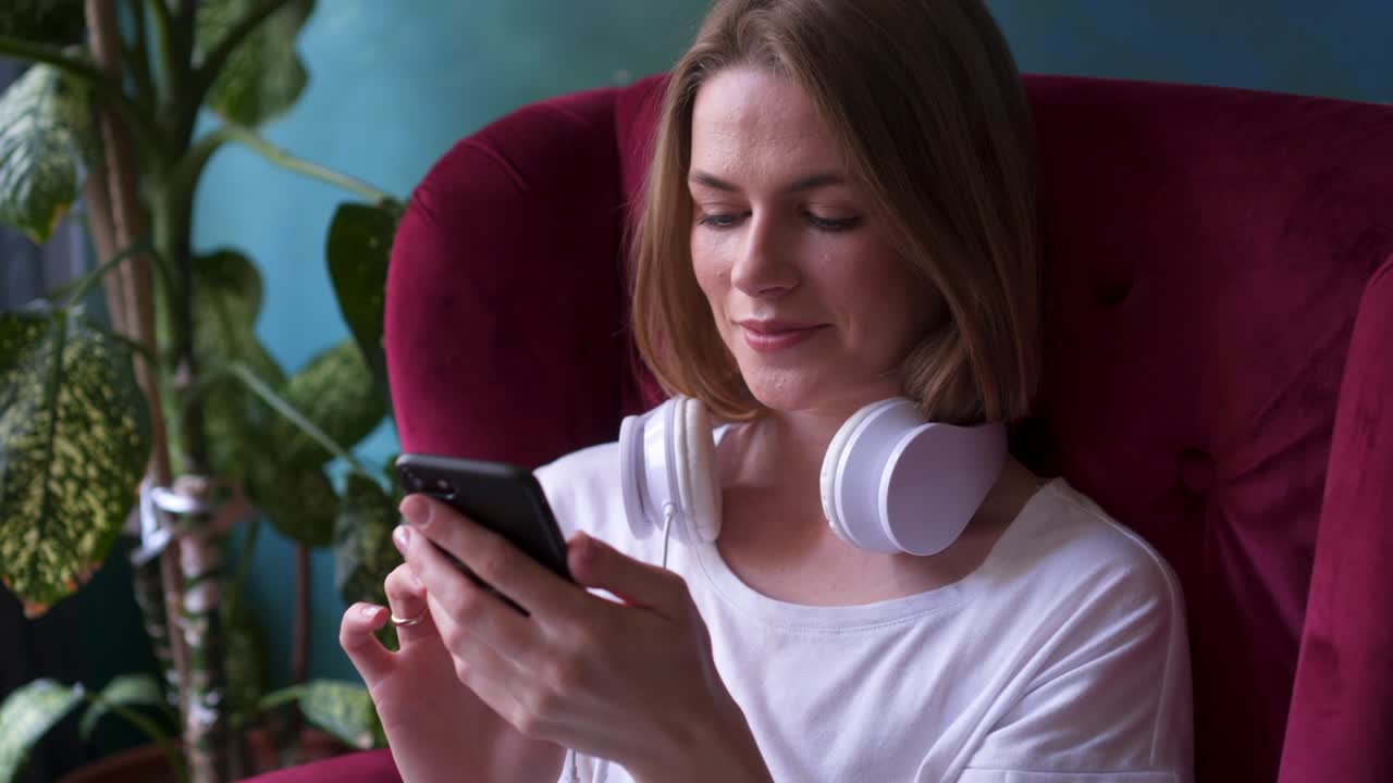 chica moderna usando el teléfono mientras está sentada en el sillón