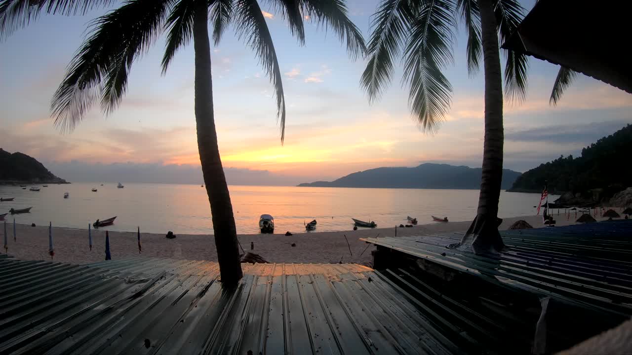 Tourist filming a colourful sunrise time lapse from a hotel balcony with a beach view on the Perhentian Islands, Malaysia. Travel concept.