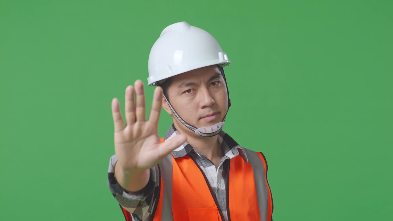 Close Up Of Asian Male Engineer With Safety Helmet Disapproving With No Hand Sign While Standing In The Green Screen Background Studio