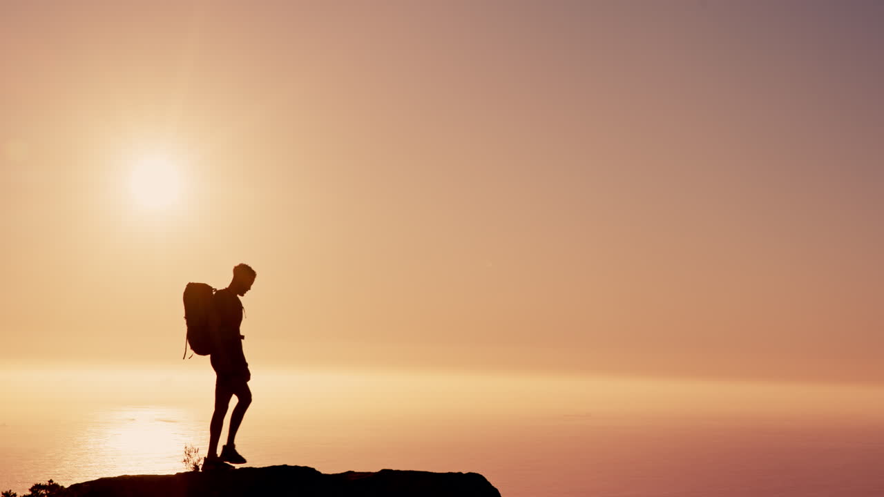hombre de pie en un acantilado con vistas al océano al atardecer