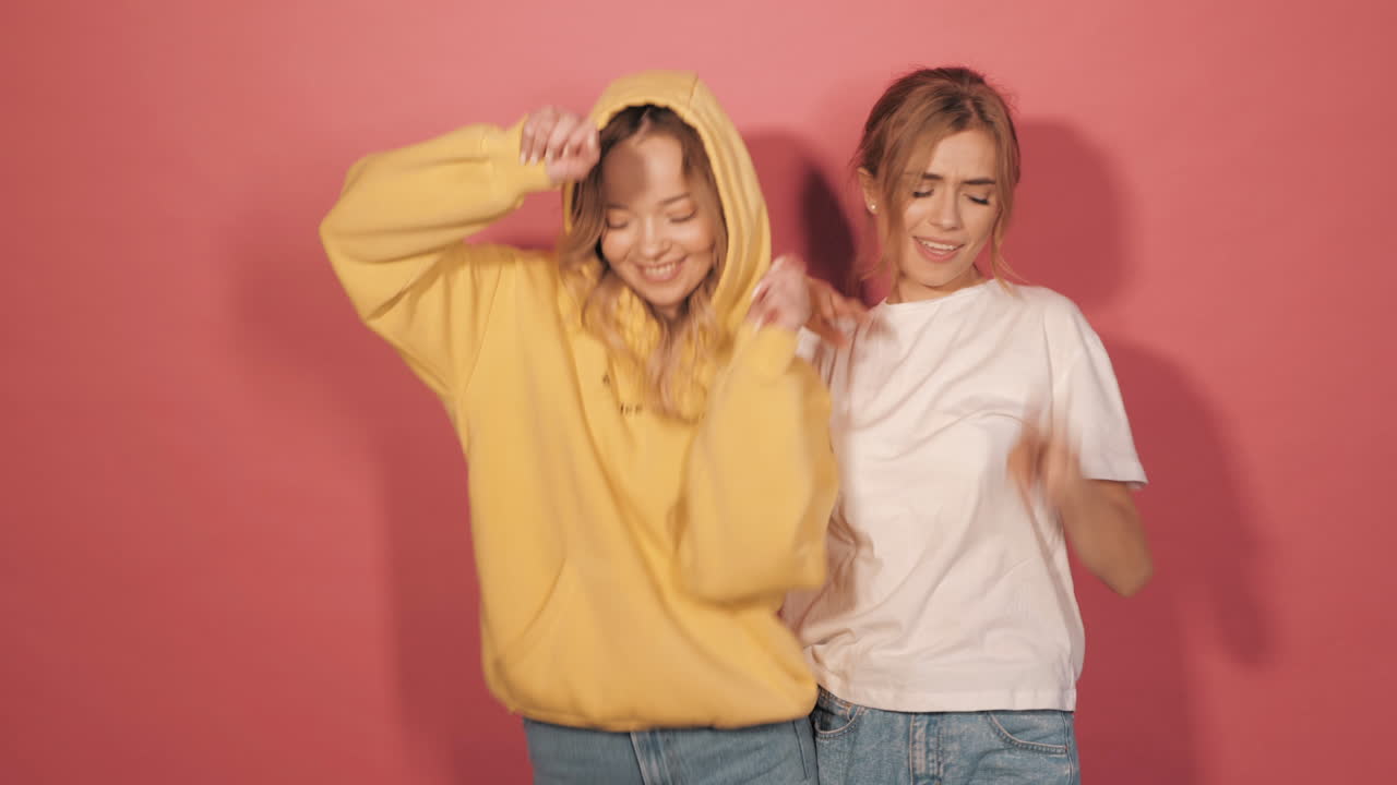 dos amigos felices bailando frente a un fondo rosado