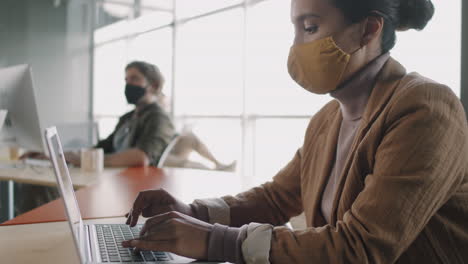 woman working on laptop in office wearing a mask during covid-19 pandemic