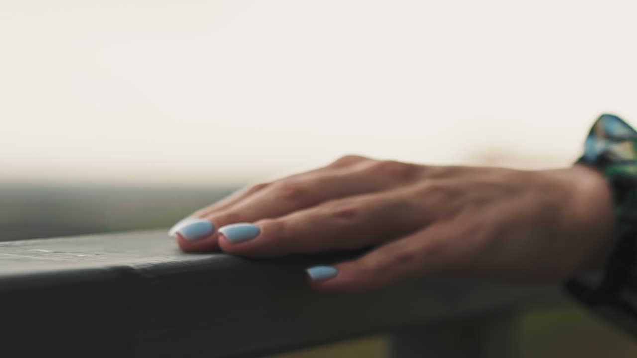 Mano di giovane donna con smalto blu scorre su una ringhiera metallica.