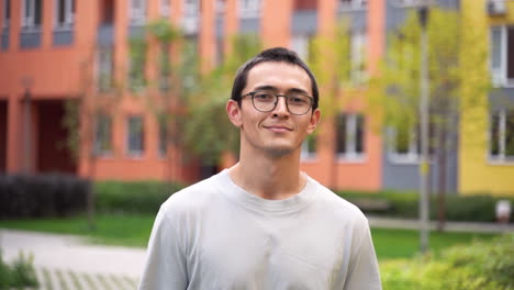 outdoor portrait of a happy japanese young man wearing eyeglasses smiling and walking towards camera