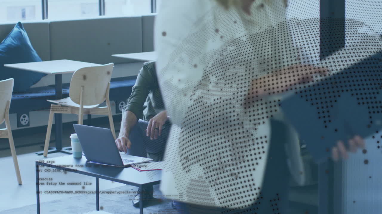 Man typing on laptop in business lounge, woman checking tablet behind dotted glass partition