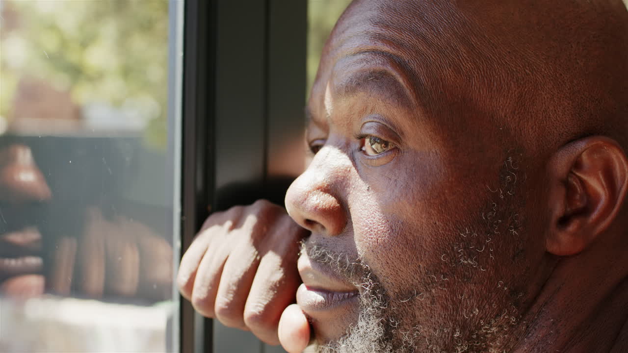 Pensive mature African American man looking out window, reflecting on thoughts and memories
