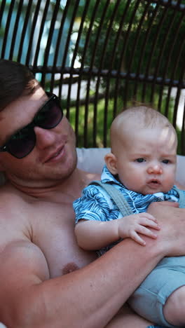 dad holding his tiny baby son and kisses him on the head. father having rest outdoors with his infant child.. vertical video