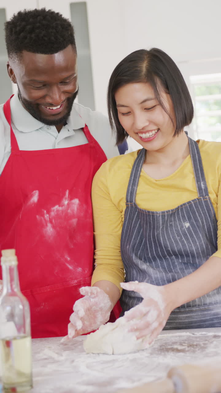 Vertical video of happy diverse couple baking in kitchen
