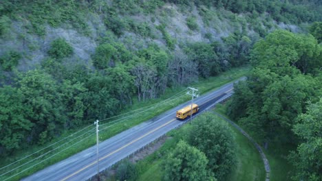 School-bus-driving-on-rural-back-road-in-mountainous-forest-land