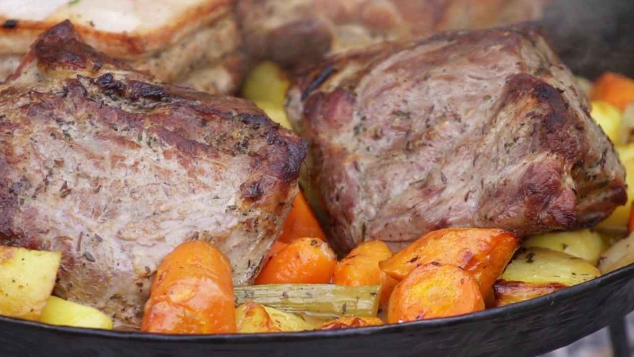 Carne arrosto succulenta e verdure colorate sfrigolano in una rustica padella di ghisa all'aperto, dorate sotto la luce naturale in questa inquadratura ravvicinata