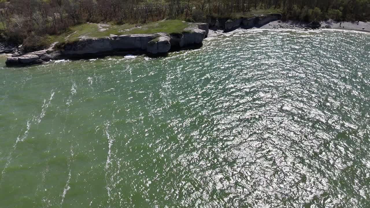 Drone che guarda in basso, poi si inclina verso l'alto e avanza verso le scogliere calcaree a Steep Rock Manitoba, rivelando la costa, gli alberi e le acque verdi del Lago Manitoba.