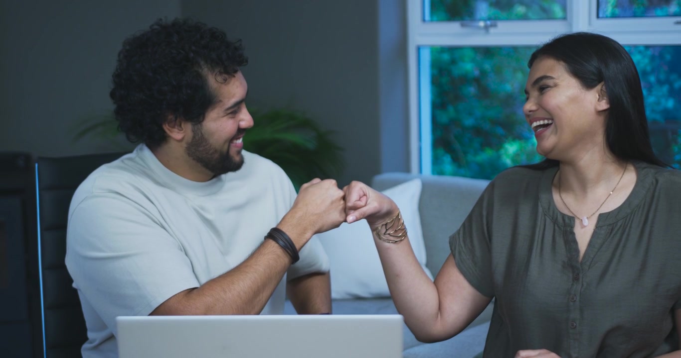 Casal jovem celebrando o sucesso com um toque de punho em casa