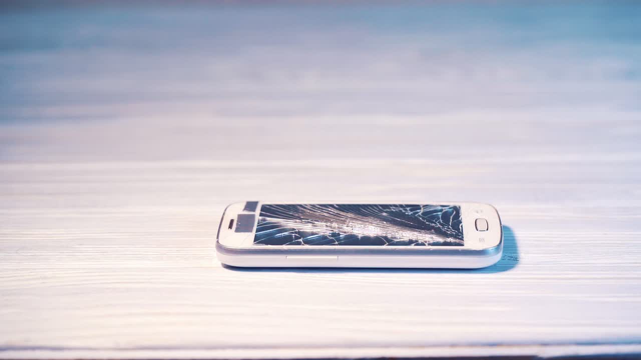 Destruction of a cell phone with a hammer. Smartphone screen cracked by hammer on floor background. Phone screen is broken