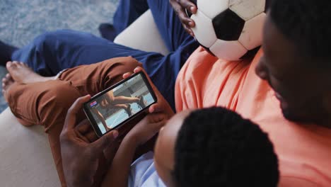 composite of father and son at home watching athletics running event on smartphone