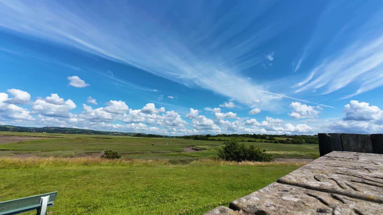 Wide Angle Timelapse of Clouds Moving Over Marshland of Loughor Estuary with Dozens of Clouds Moving and Growing Across Blue Sky Background. Sitting Bench for View in Foreground