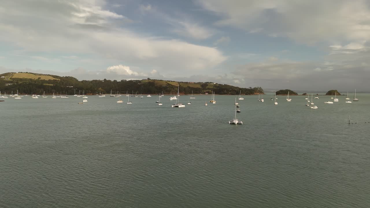 Sailing boats and yachts on water bay of Shelly Beach at sunset. Aerial orbit wide shot. New Zealand with clouds at sky.