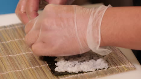 mani veloci che spalmano riso di sushi su un involucro di nori con un tappetino di bambù sotto - up close