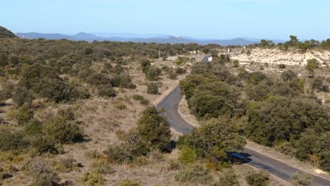 Aerial-view-above-jeep-driving-over-road-through-the-southern-France-countryside,-wilderness