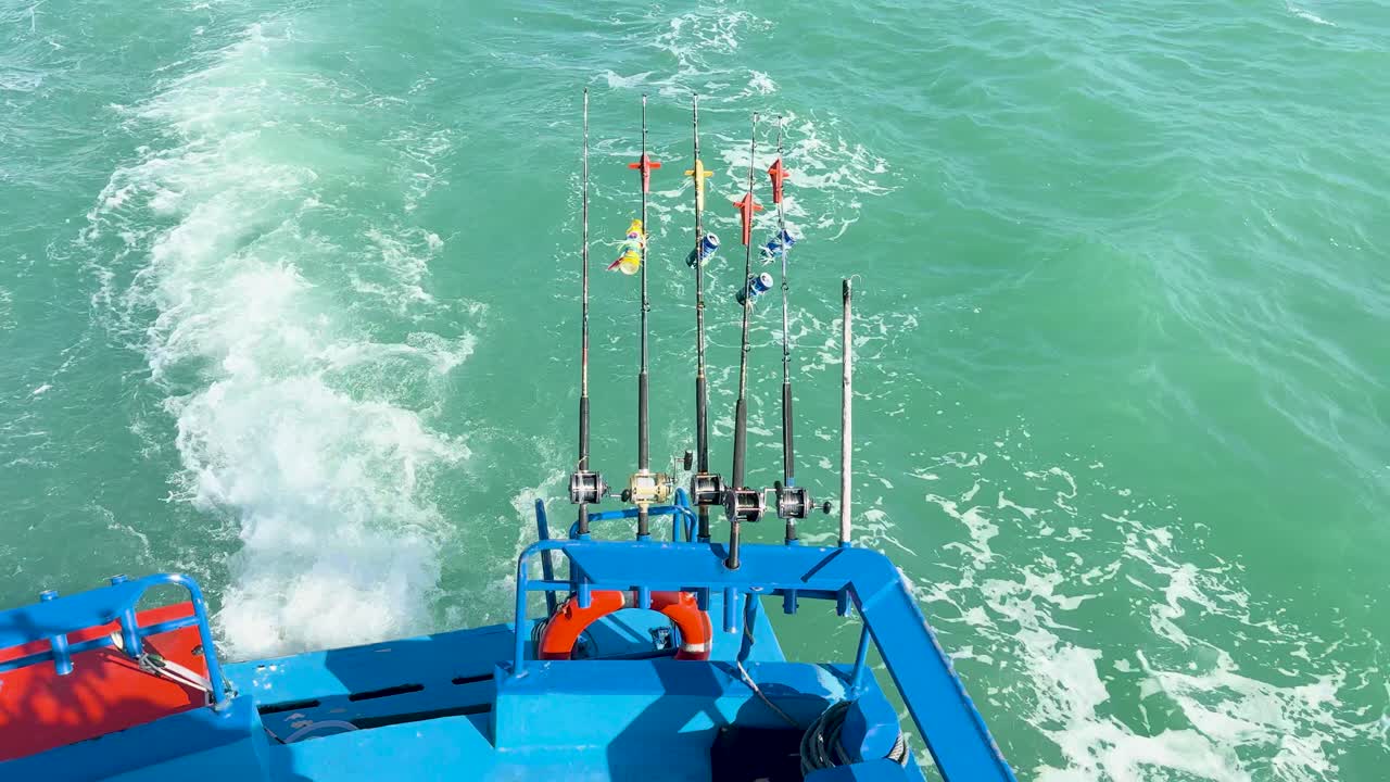 A vibrant fishing boat with multiple rods cuts through turquoise waters, creating a dynamic wake under bright sunlight