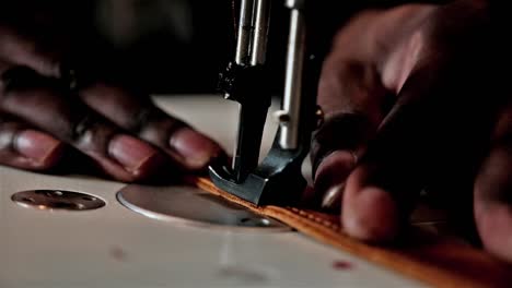 Close-up-of-a-black-hand-using-a-sewing-machine-to-sew-leather-with-mechanical-needle-and-thread