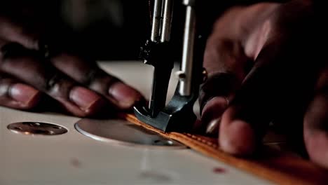 close up of a black hand using a sewing machine to sew leather with mechanical needle and thread