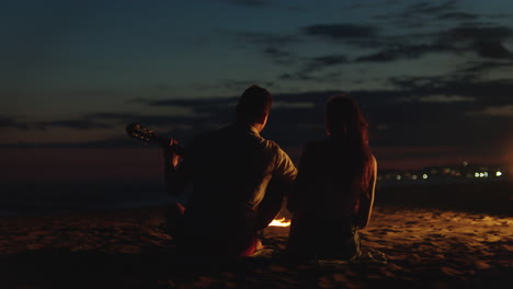 couple playing guitar by the campfire on the beach at night