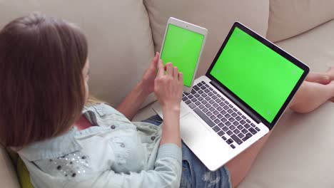 hermosa chica usando una tableta pc y una computadora portátil con pantalla verde pre-enclavada sentada en el sofá en casa.