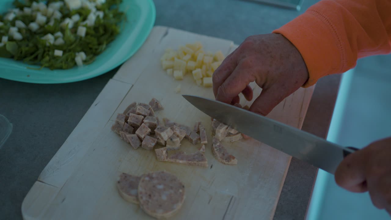 cortando una salchicha en una tabla de madera y añadiéndola a una ensalada
