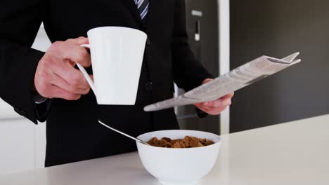 hombre de negocios leyendo el periódico mientras toma café en la cocina