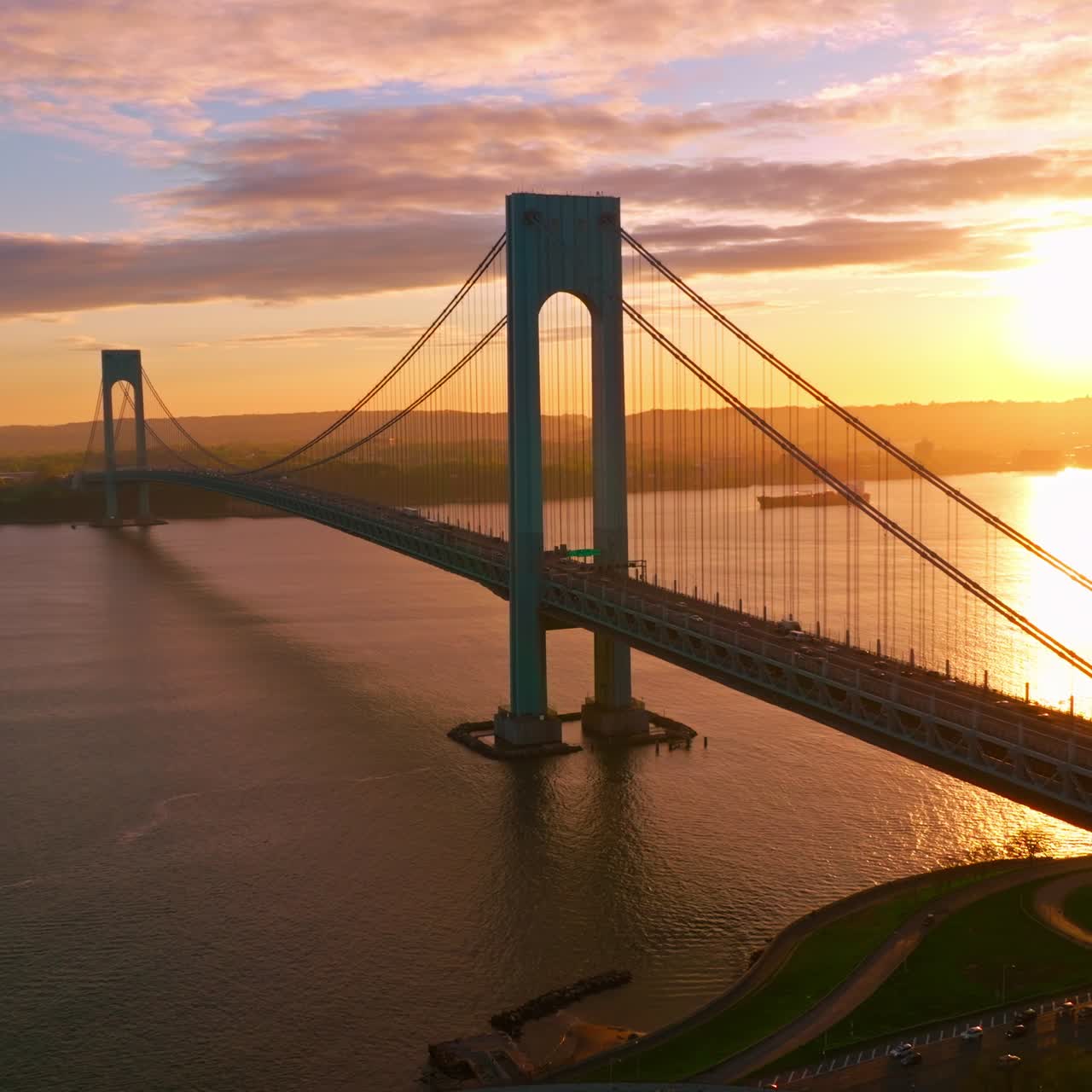 Whitestone Bridge over East River at setting sun. Sun reflecting in the calm water. Non-stopping traffic of New York