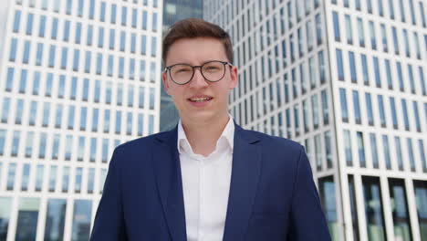 A-young-successful-businessman-smiles-into-the-camera-in-front-of-the-modern-office-building