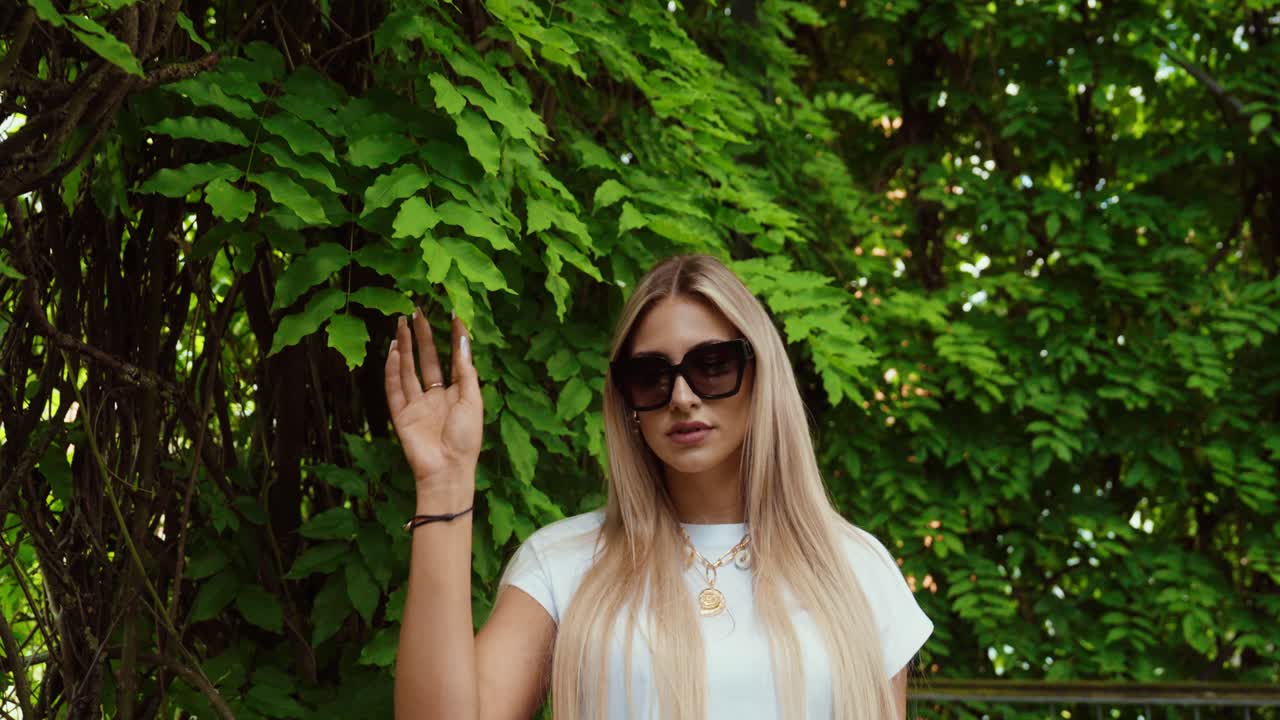 beautiful woman in a park between the trees and the leaves.she touches the plants with one hand