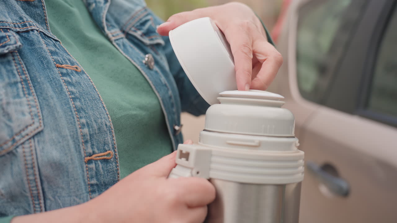 Woman Drinks Warm Beverage, Woman Pours Hot Drink Carefully, Individual Transfers Warm Liquid Into Small Vessel, Caregiver Gently Pours Steaming Drink Into Mug During Travel Break Outside
