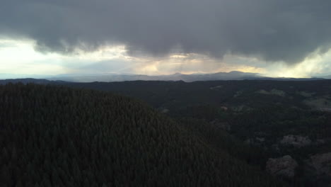 aerial view of storm clouds looming in the distance in the forested mountains of colorado, tilt down, backwards motion