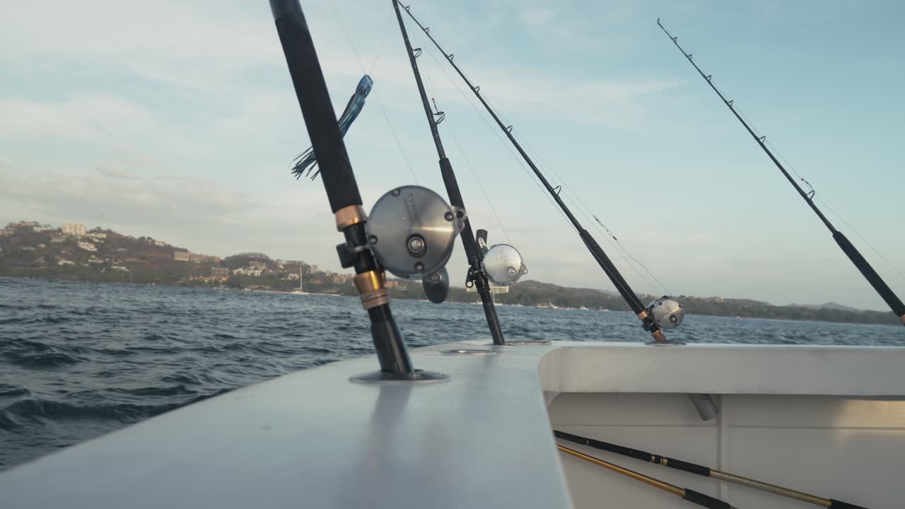 Close-up of multiple fishing rods mounted on boat in motion across tranquil ocean.