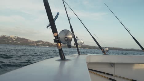 close-up of multiple fishing rods mounted on boat in motion across tranquil ocean.