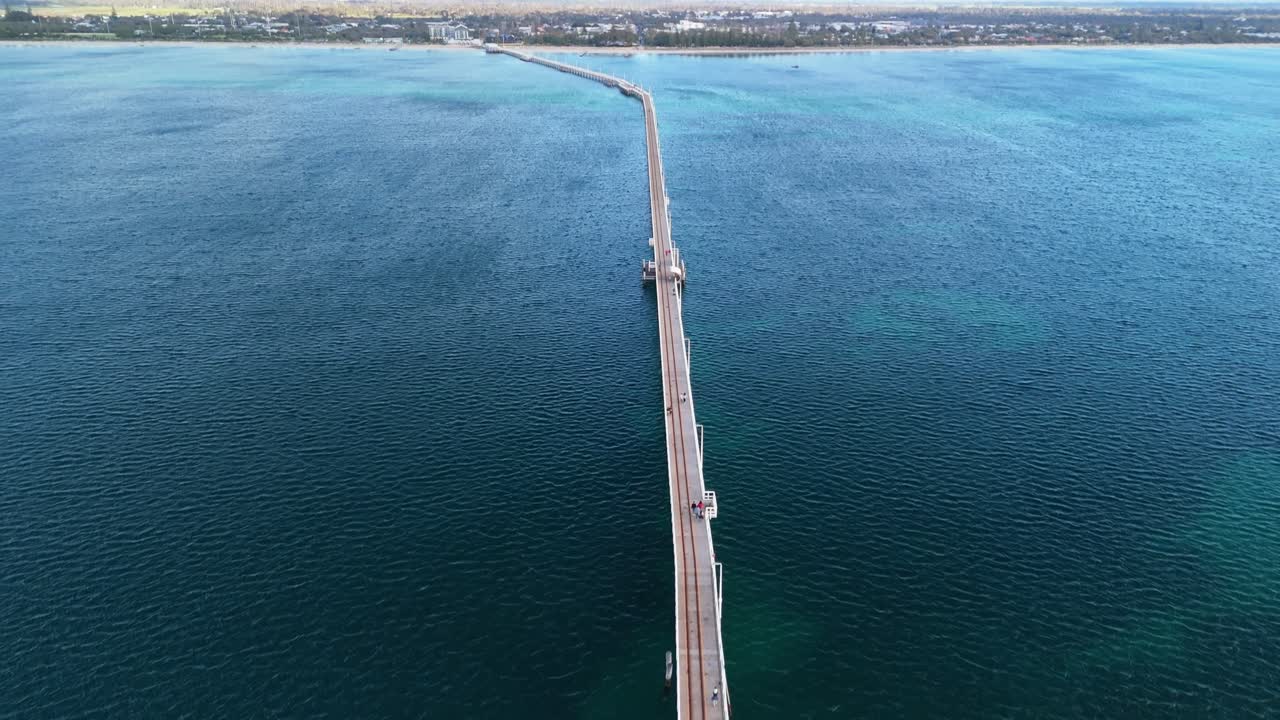 drone flying above train along Busselton Jetty in Western Australia tilting up to reveal the town
